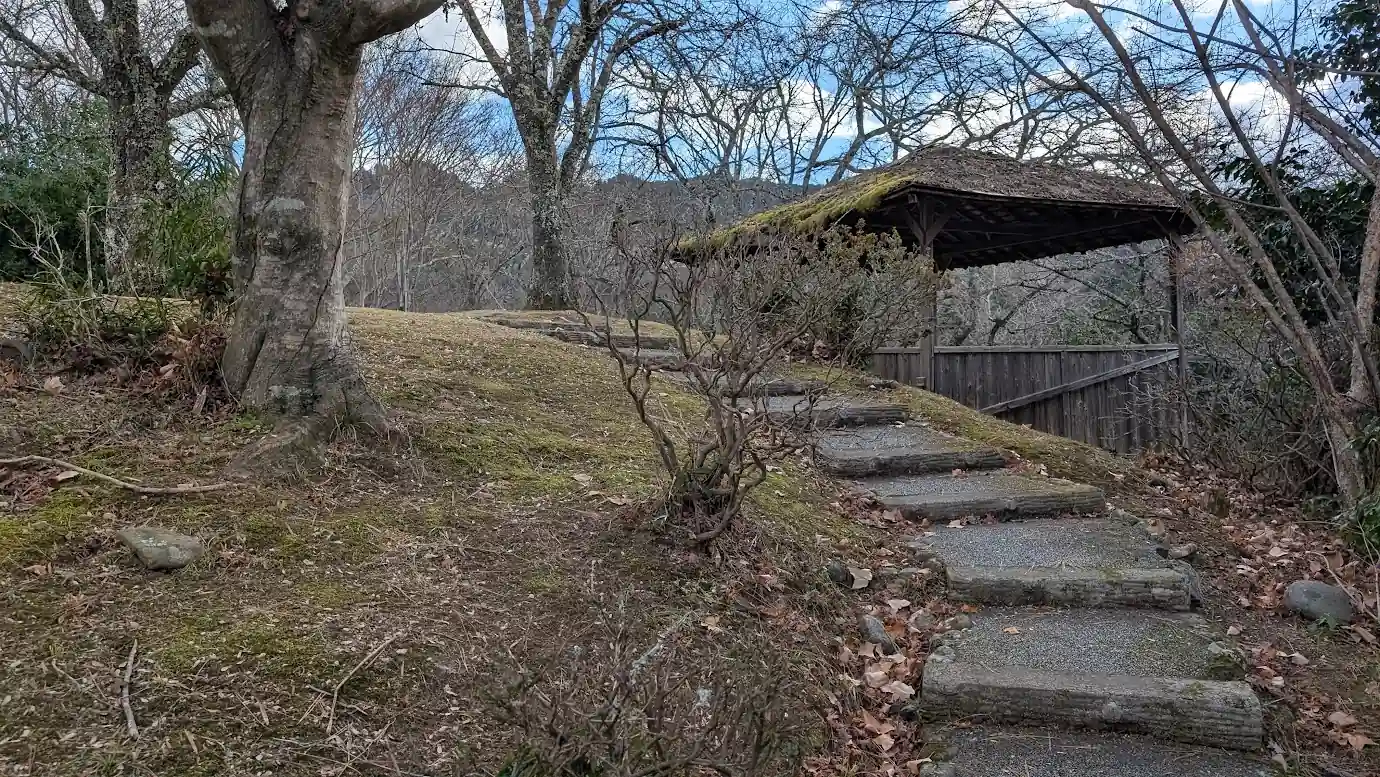 竹林院群芳園の庭園内。苔むした丸太の階段を上った先にある趣深い東屋(あずまや)と、木々の向こうに吉野の山並みを取り込んだ借景の風景
