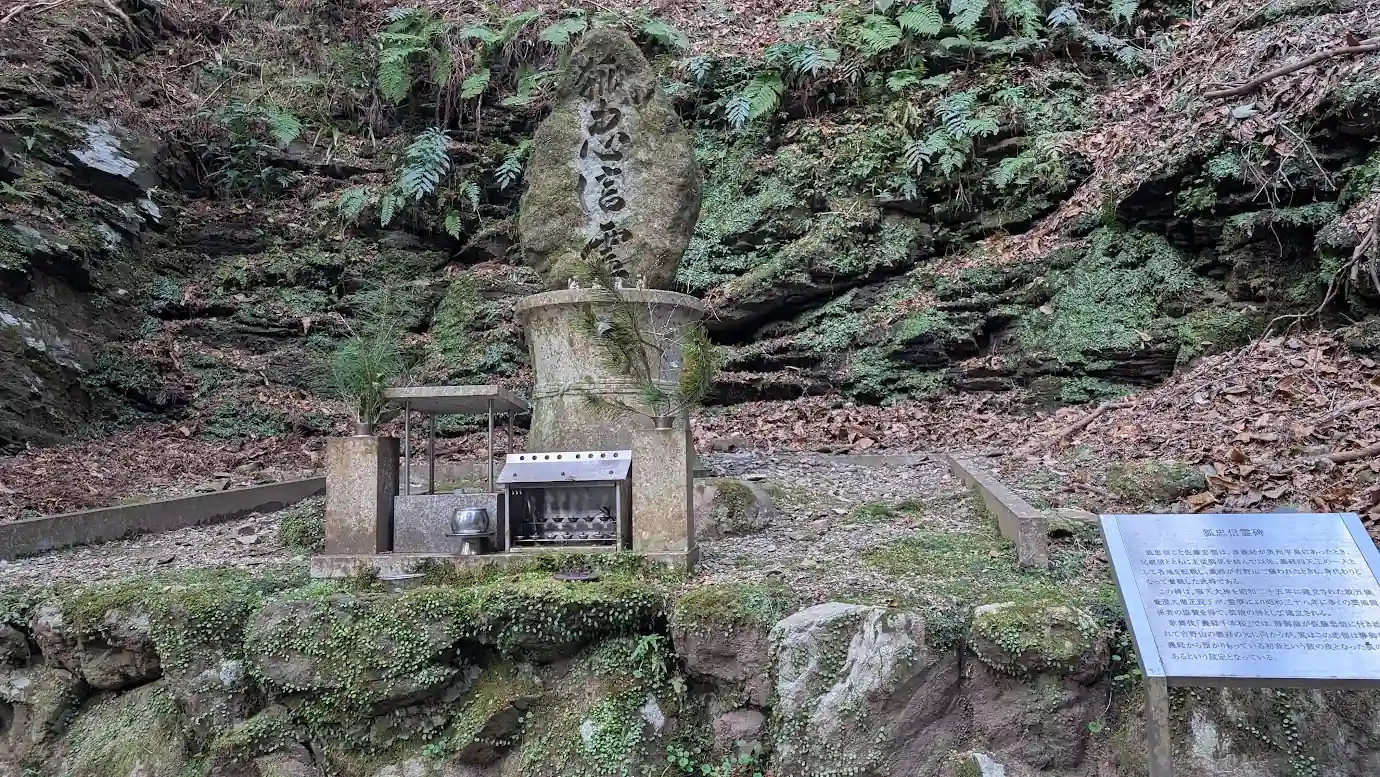 脳天大神への道中にある「狐忠信霊碑」の全体写真。岩肌を背にした大きな石碑と、右側に設置された由緒書きの解説板の風景。