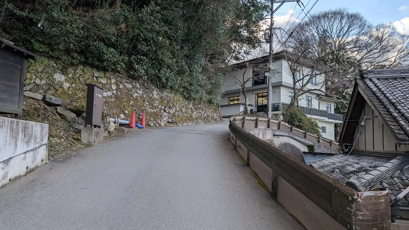 金峯山寺の仁王門前を右折した直後の上り坂の様子。左手に古い石垣、右手にガードレールが続く細い舗装路。