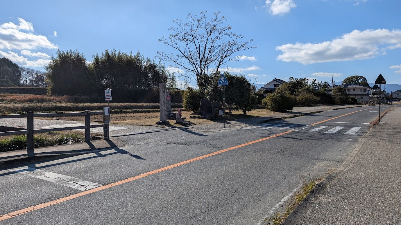 奈良県明日香村、石舞台古墳方面から橘寺へ続く道路。前方に横断歩道と、左手に橘寺の入り口を示す案内看板や石碑が見える分岐点の風景（2026年1月12日撮影）。