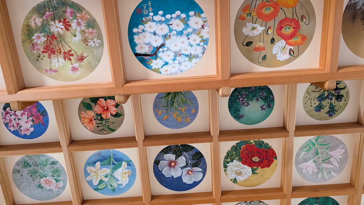 奈良県明日香村の橘寺、往生院の天井画。格子状の天井（格天井）の円形スペースに、蓮、牡丹、菊など、様々な種類の花が色鮮やかに描かれた、複数の天井画のアップ（2026年1月12日撮影）。