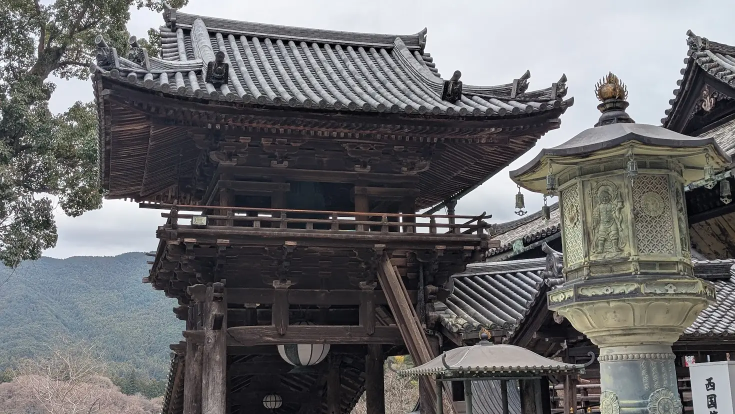 奈良県桜井市・長谷寺の重要文化財である鐘楼。重厚な木造二階建ての造りで、手前には精巧な彫刻が施された石灯籠が写っている冬の風景。