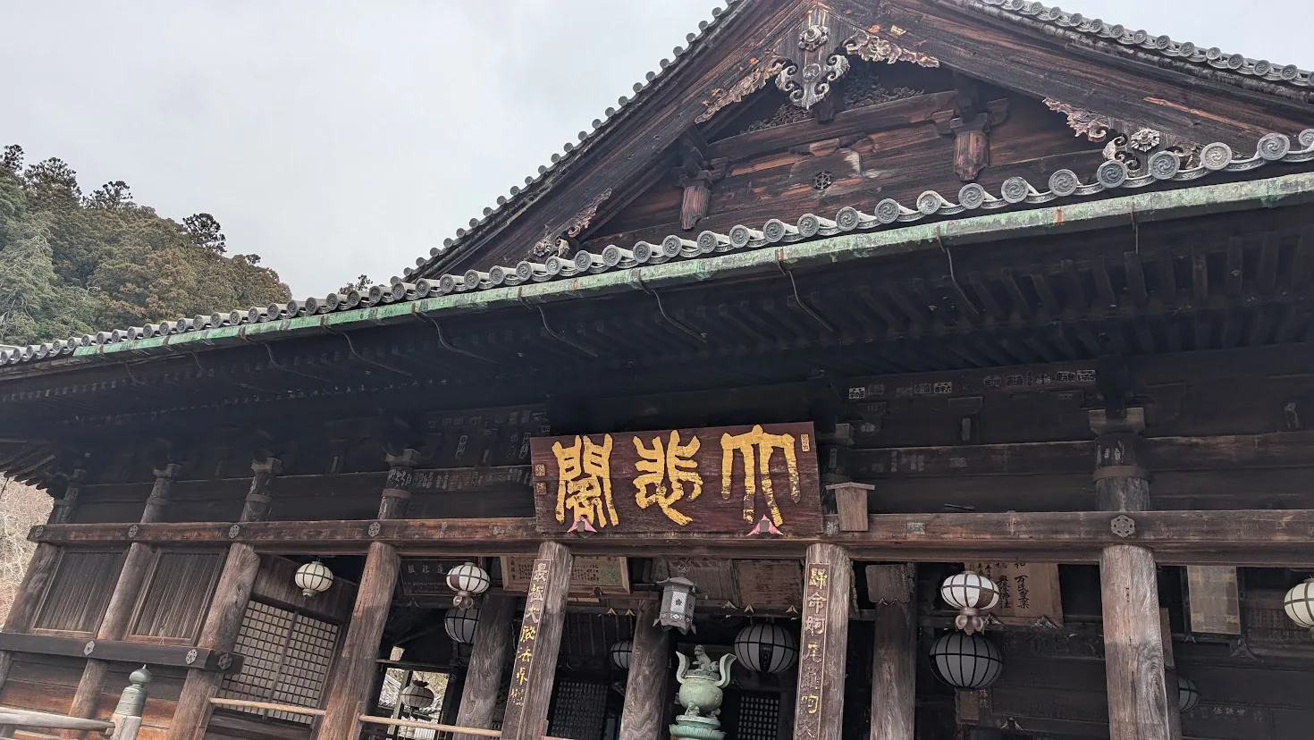 長谷寺の本堂（舞台）から見下ろした冬の境内の風景。木造の舞台の縁越しに、山あいに広がる寺院の建物や瓦屋根、澄んだ冬の空が広がっている。