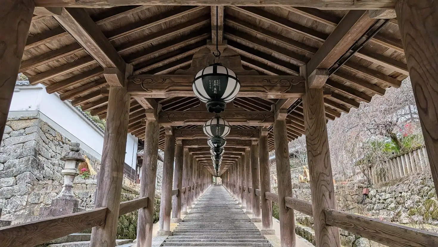 奈良県桜井市・長谷寺の重要文化財「登廊（のぼりろう）」。屋根付きの長い石段が上へと続き、天井からは等間隔に美しい灯籠が吊るされている正面からの風景。