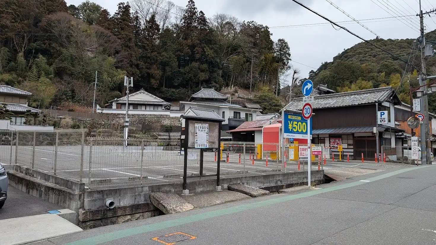 長谷寺まで徒歩8分の場所にある、広々とした舗装済みのコインパーキング。入口にはゲート（バー）があり、料金看板には「500円」と大きく表示されている。周囲は静かな住宅街と山々に囲まれている。