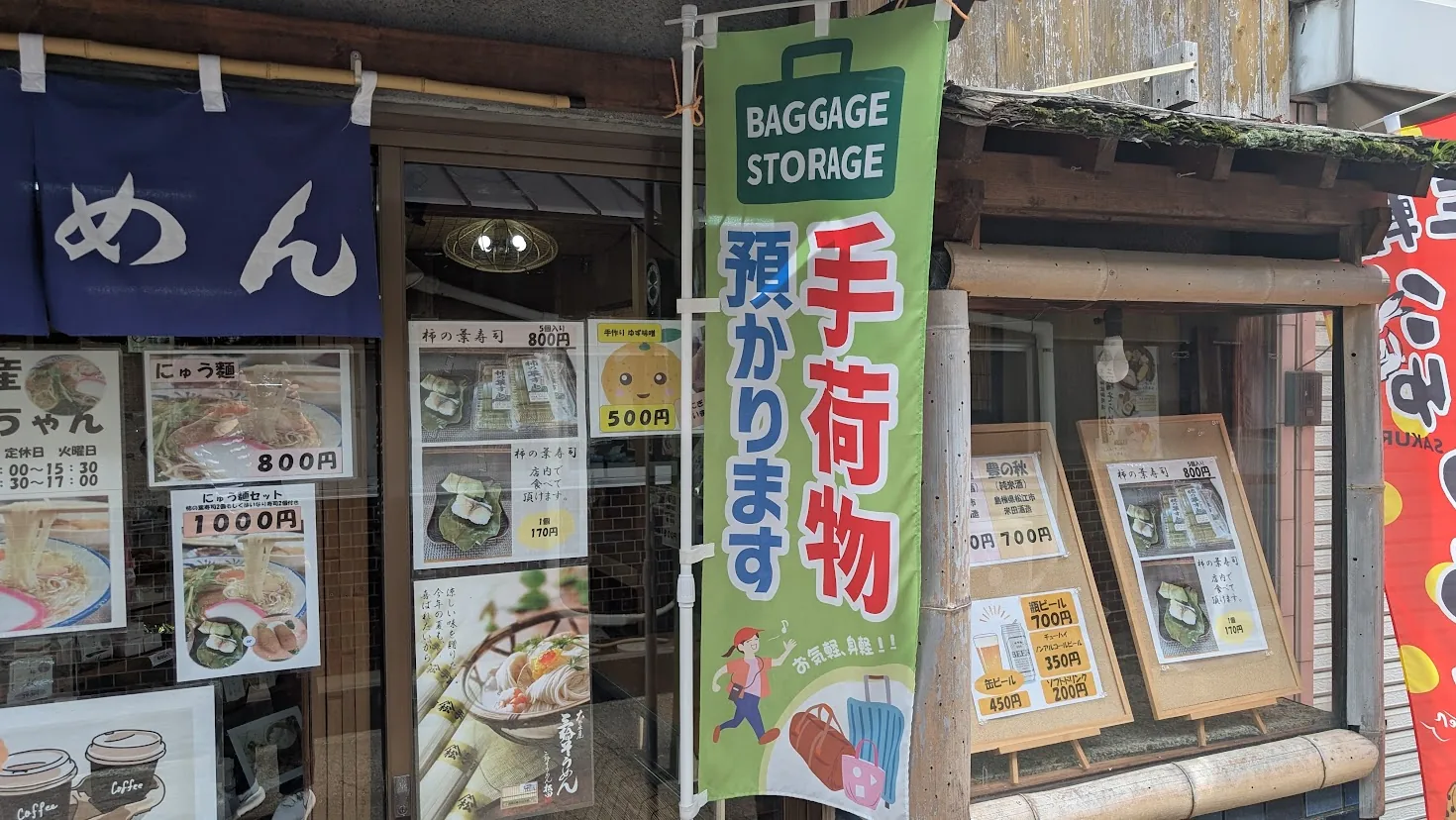 JR三輪駅すぐの店舗前に立つ「手荷物預かります」と書かれた緑色ののぼり旗。