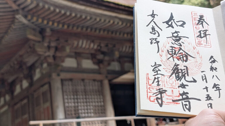 奈良県宇陀市の室生寺。手前に「如意輪観世音」と墨書きされた御朱印帳を持ち、背景には国宝の本堂（灌頂堂）が美しい檜皮葺の屋根とともに写っている（2026年1月15日拝受）。