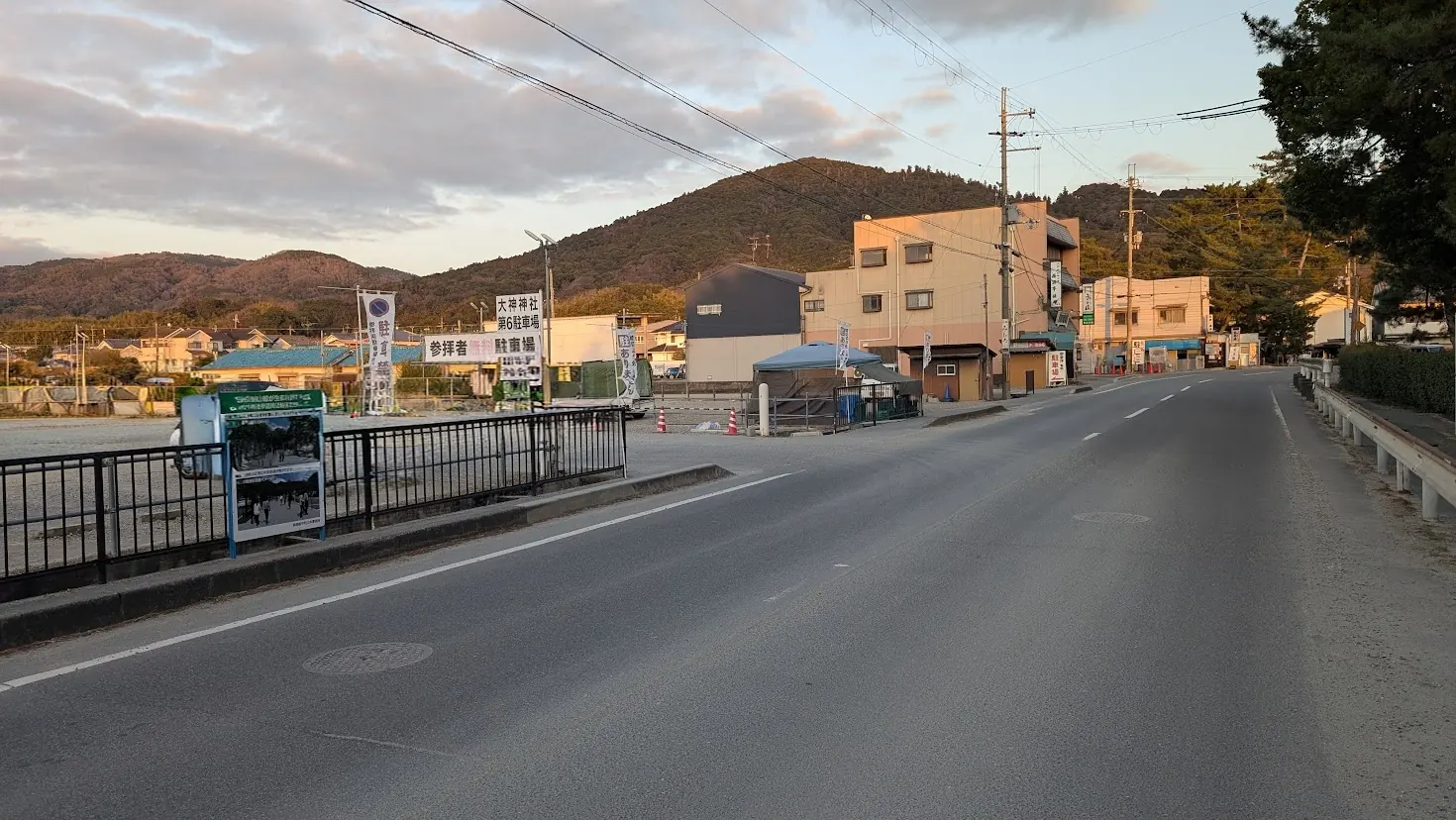 夕暮れ時、三輪山を背景にした大神神社の広い第六駐車場の風景。周囲の道路や住宅が見える全景。