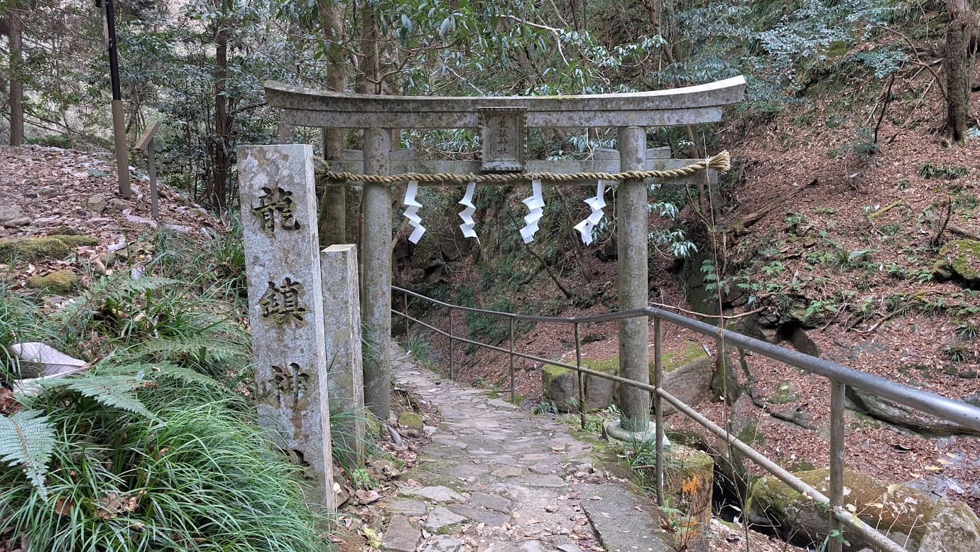 奈良県宇陀市の龍鎮神社。山道を抜けた先に現れる石造りの第二鳥居と「龍鎮神社」と深く刻まれた立派な社号標。鳥居の先には下り階段が続いている。
