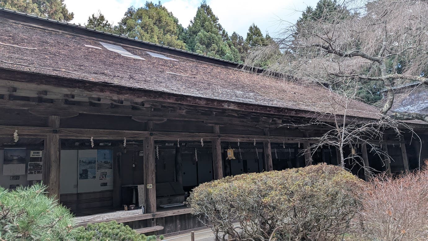 奈良県吉野町、世界遺産・吉野水分神社の拝殿と回廊。厚みのある茅葺屋根が長く伸び、木の質感が美しい柱が整然と並んでいる。奥には幣殿が見え、手前には冬の植栽が配置された静謐な境内の風景（2026年1月撮影）。