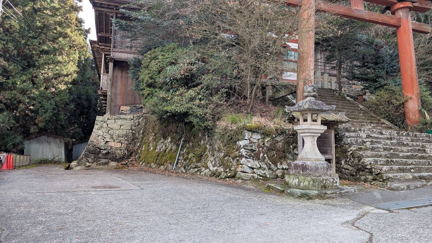 奈良県吉野町、吉野水分神社の鳥居のすぐ左横にあるアスファルト舗装された駐車スペース。石灯籠の影に数台停められる広さがあり、背後には神社の古い石垣が組まれている冬の風景(2026年1月撮影)。