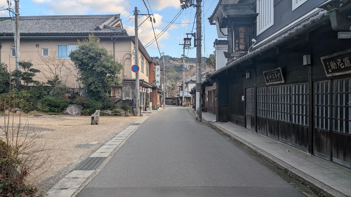 奈良県吉野町、吉野山のメイン通り（門前町）。右側には伝統的な木造建築の商店が並び、「陀羅尼助」の看板が見える。電柱が立ち並び、奥へと続く静かな1車線の道路（2026年1月撮影）。