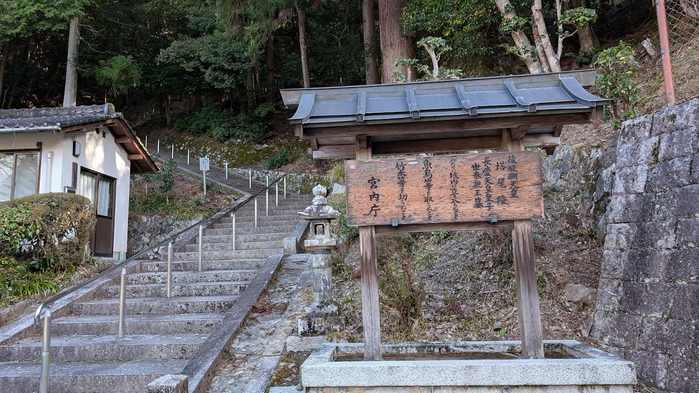 奈良県吉野町、如意輪寺の奥にある後醍醐天皇の御陵(塔尾陵)の案内板。木製の掲示板に「後醍醐天皇 塔尾陵」「宮内庁」と墨書きされ、背後には山の上へと続く長い石段が伸びている冬の風景(2026年1月撮影)。