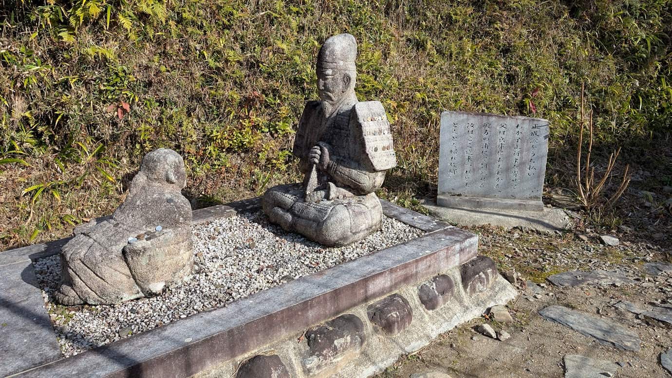 奈良県吉野町、如意輪寺の境内にある楠木正成と正行父子の石像。甲冑姿の父・正成が息子・正行に教訓を授けている場面を再現している。横には「正成公をうち払い…」と記された石碑が立っている(2026年1月撮影)。