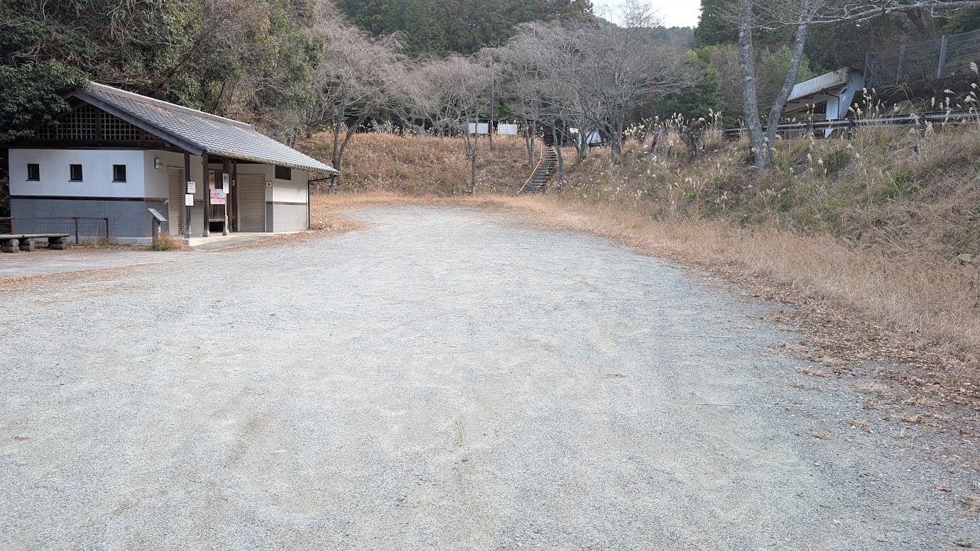 奈良県吉野町、如意輪寺の無料駐車場。地面は砂利と土の未舗装で、駐車の区画線はない。奥には公衆トイレの建物が見え、冬の木々に囲まれた静かな駐車スペース（2026年1月撮影）。