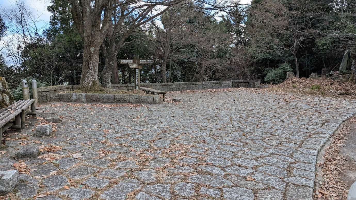 奈良県吉野町、奥千本にある高城山展望台の入口広場。石畳が敷き詰められ、周囲には低い石垣と木のベンチが配置されている。中央には「高城山展望台」と記された木製の案内標識が立っている冬の風景(2026年1月撮影)。