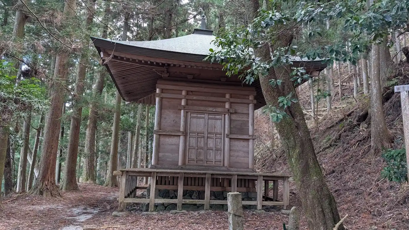 杉の巨木に囲まれた、質素ながら力強い木造建築の義経隠塔(蹴抜の塔)の全景