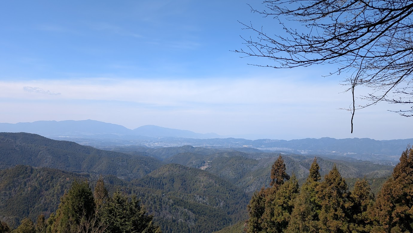 奈良県黒滝村の鳳閣寺にある展望デッキからの眺め。幾重にも連なる山並みの先に吉野山が見え、遠くに金峯山寺の大きな屋根が確認できる。澄み渡った空と深い緑の対比が美しい。