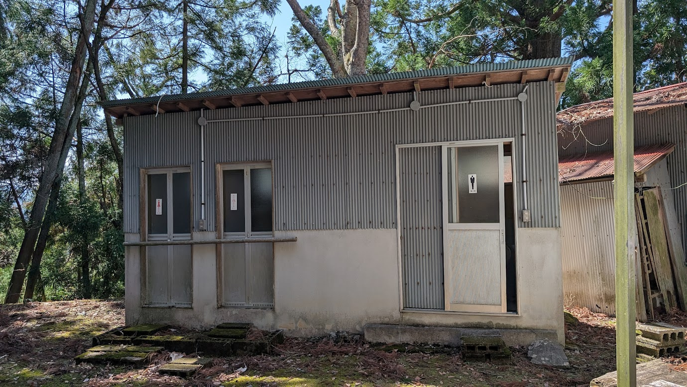 鳳閣寺の境内裏手にある古い平屋のトイレ。トタン壁の簡易的な造りで、周囲には落ち葉が積もっている。現在は使用が推奨されない状態。
