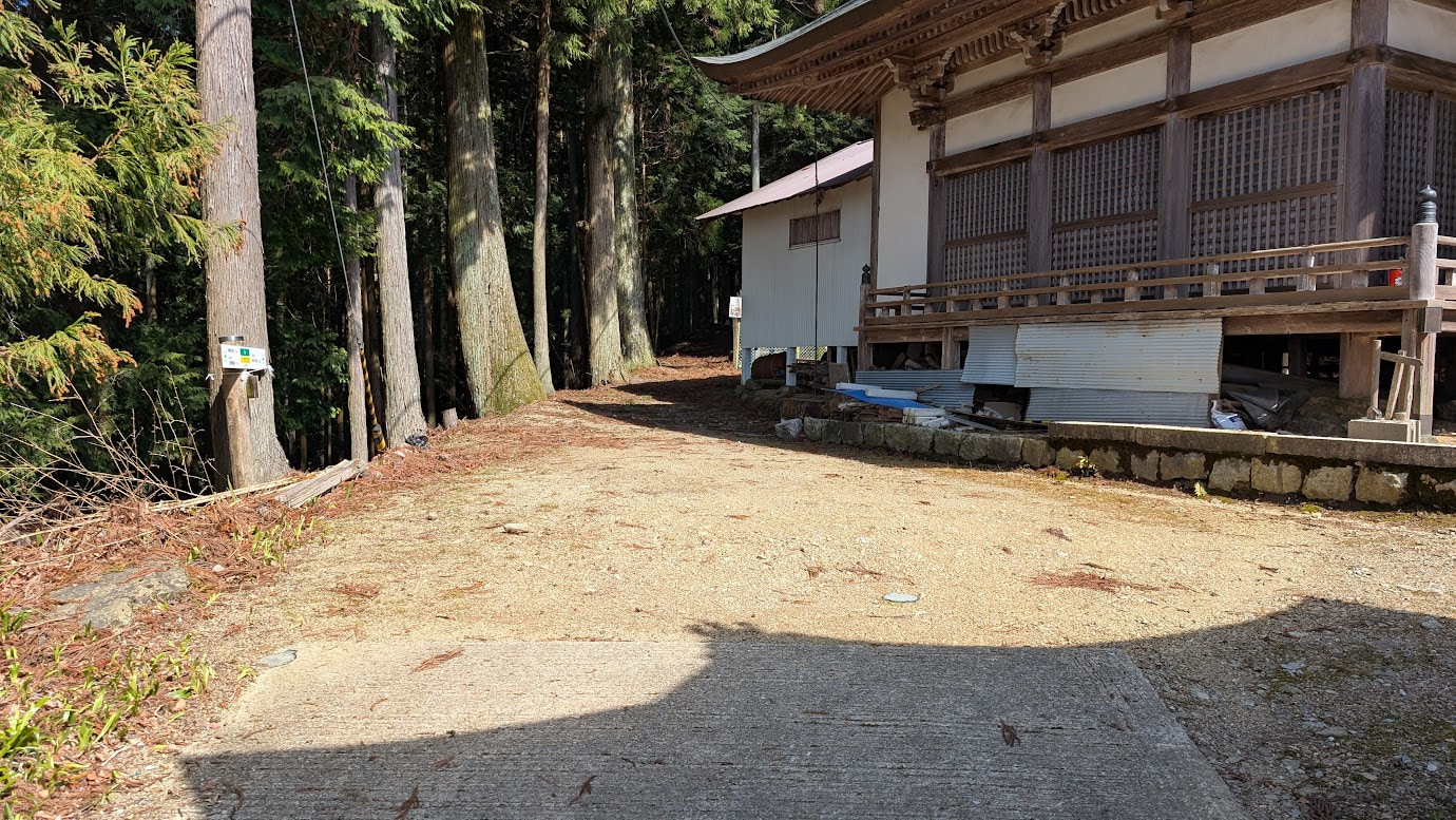 奈良県黒滝村の鳳閣寺境内。木造の社殿のすぐ横に平坦な砂利のスペースがあり、周囲は高い杉の木々に囲まれている。車が数台停められる程度の広さ。