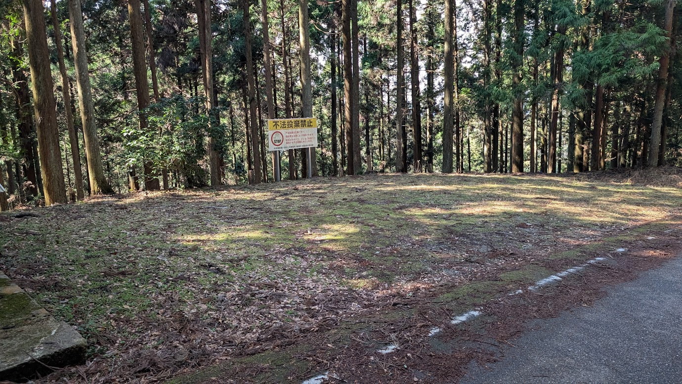 奈良県黒滝村、鳳閣寺の下にある地蔵堂のすぐ横に広がる駐車スペース。地面は苔と落ち葉に覆われており、奥には「不法投棄禁止」の看板と深い杉林が広がっている。