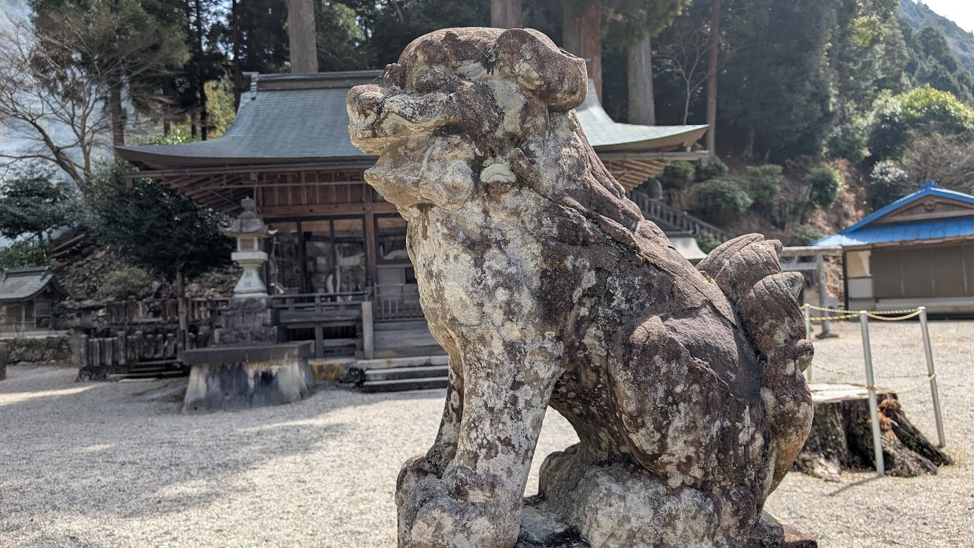奈良県黒滝村の河分神社。手前に苔むした石造りの狛犬が鎮座し、奥に木造の拝殿が見える。木漏れ日が地面の苔を照らしている。