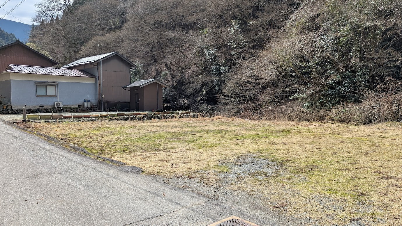 奈良県黒滝村の河分神社近くにある、砂利と草の広がる空き地。背後には山肌と民家が見える。