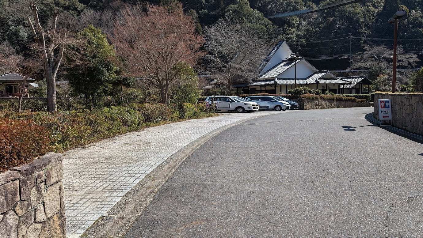奈良県黒滝村、旧役場庁舎（文化保存伝習館）の正面にある駐車スペース。石畳の歩道とアスファルトの道がカーブしており、奥には白壁の和風建築と数台の乗用車が停まっている。トイレの案内板も見える。
