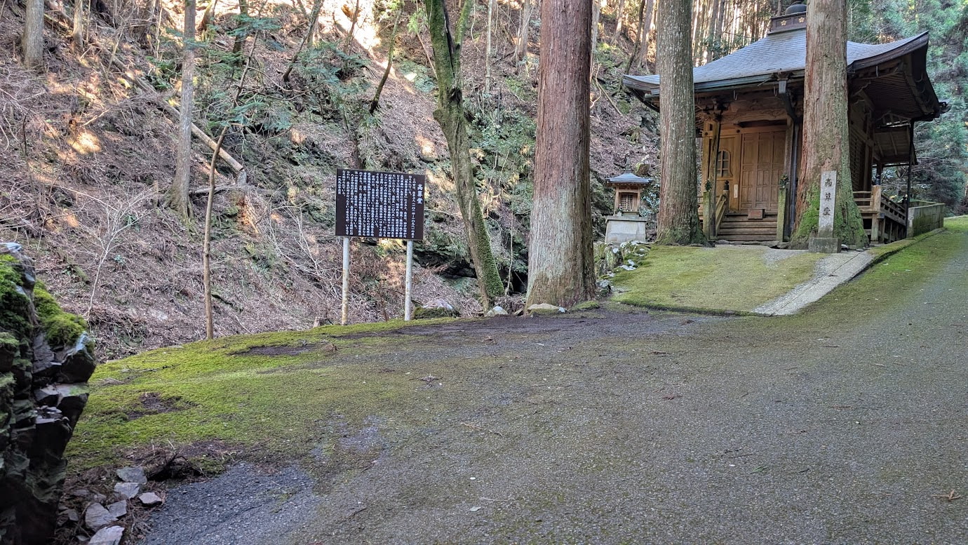 奈良県黒滝村、瀧光寺の高算堂の目の前にある駐車スペース。アスファルトの道の脇に苔が生えた平坦な場所があり、すぐ奥に高算堂と解説板、巨木が立っている。