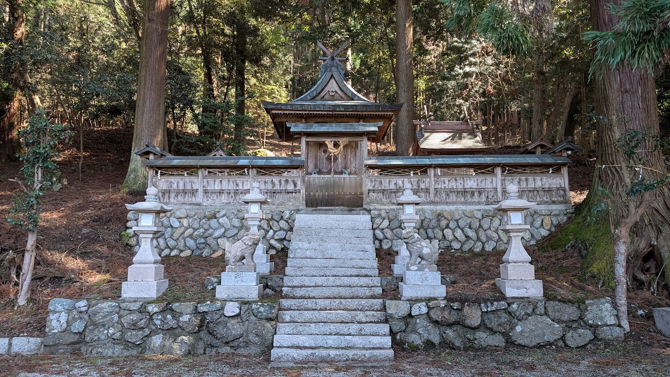 奈良県黒滝村、鳥住春日神社の本殿。美しい石垣の上に木造の社殿が立ち、手前には一対の石灯籠と小さな狛犬、石段がある。背景には深い杉林が広がっている。