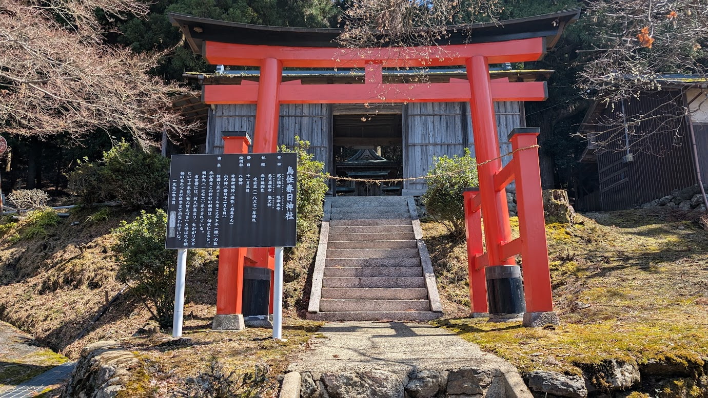 奈良県黒滝村にある鳥住春日神社の入り口。鮮やかな朱色の鳥居が立ち、左手には由緒が記された解説板がある。石段の先には木造の社殿が見える。