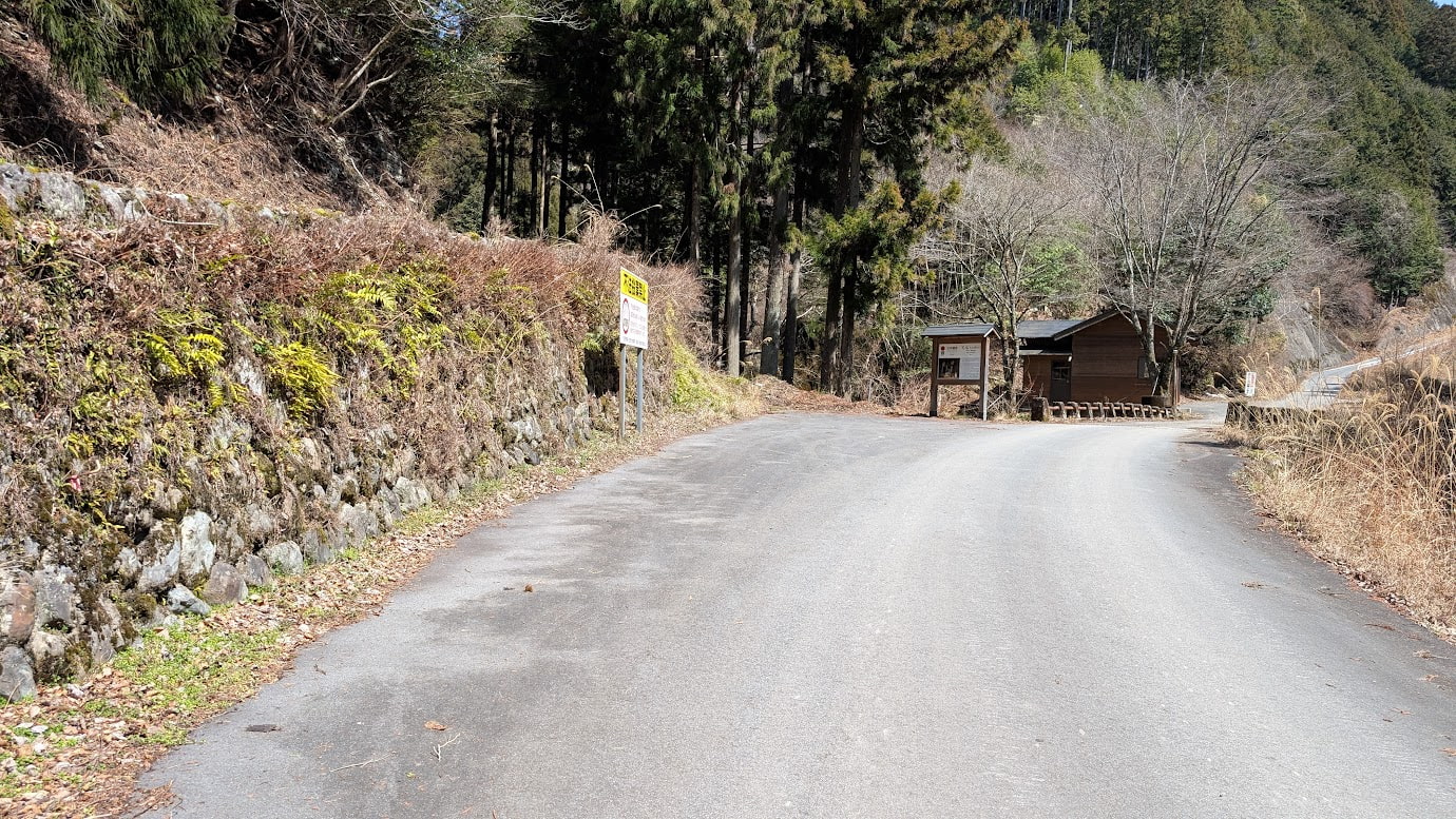 奈良県黒滝村、日本遺産「石仏」の近くにある駐車スペース。道路脇にアスファルトで舗装された数台分のスペースがあり、すぐ横を川が流れている。背景には深い緑の山々が見える。
