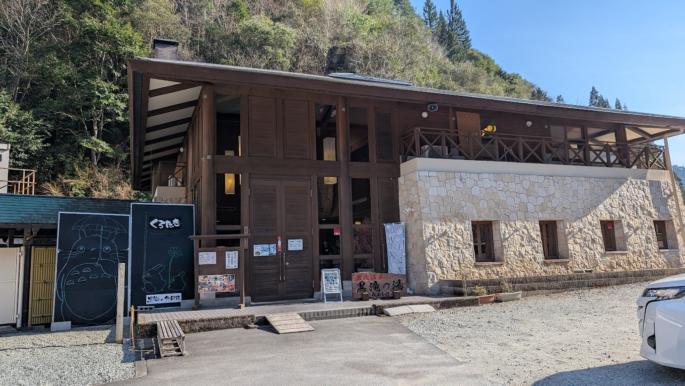 奈良県黒滝村にある日帰り温泉施設「黒滝の湯」の外観。木造と石造りが組み合わさったモダンな建物で、入り口横には黒板に描かれたトトロのイラストがある。
