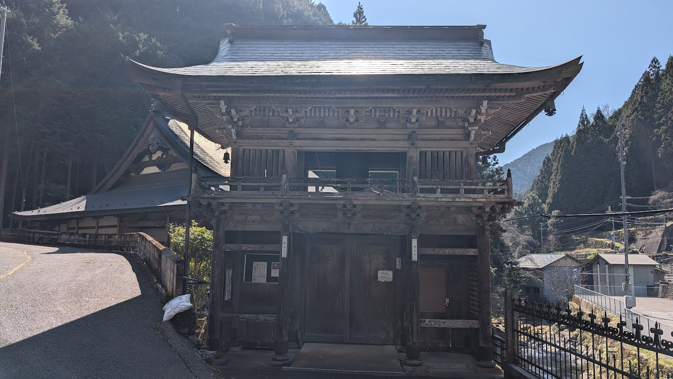 奈良県黒滝村にある瀧光寺の山門。石垣の上に瓦屋根の木造門が建っており、奥には本堂の大きな屋根が見える。周囲は深い杉林に囲まれている。