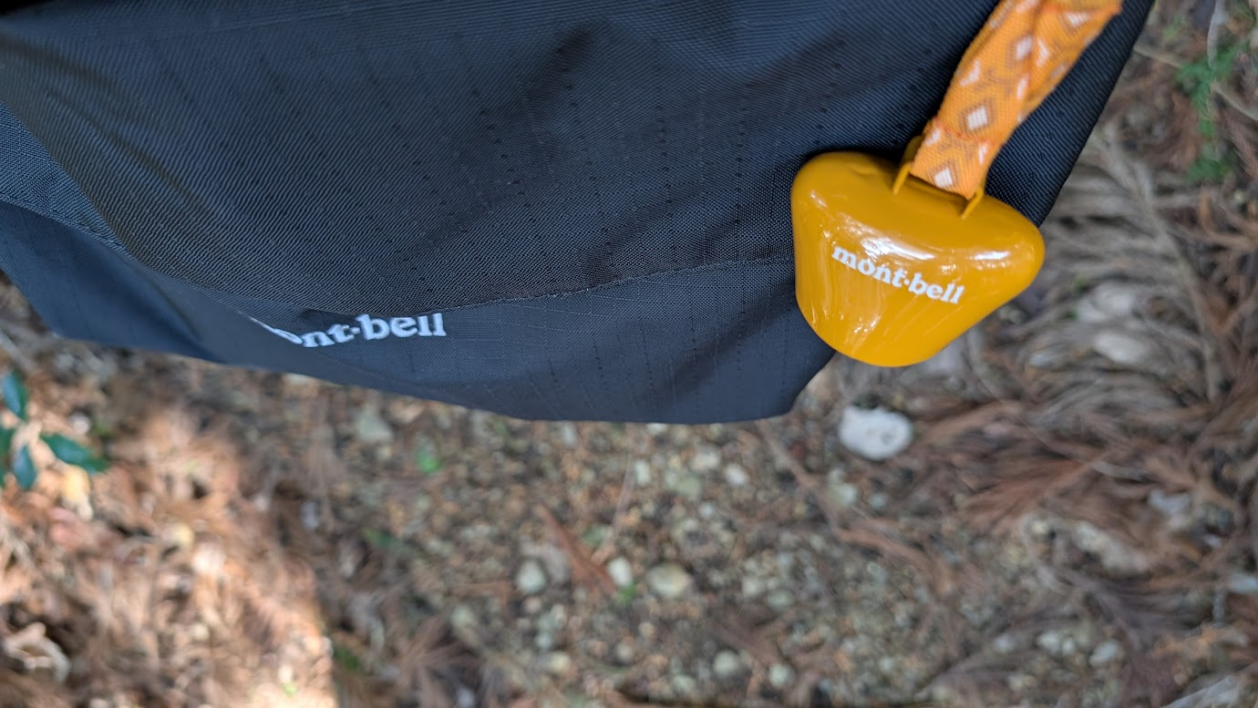 鳳閣寺への山道で、モンベルのバックパックに付けられたオレンジ色の熊鈴。背景には落ち葉が積もった地面がボケて写っている。