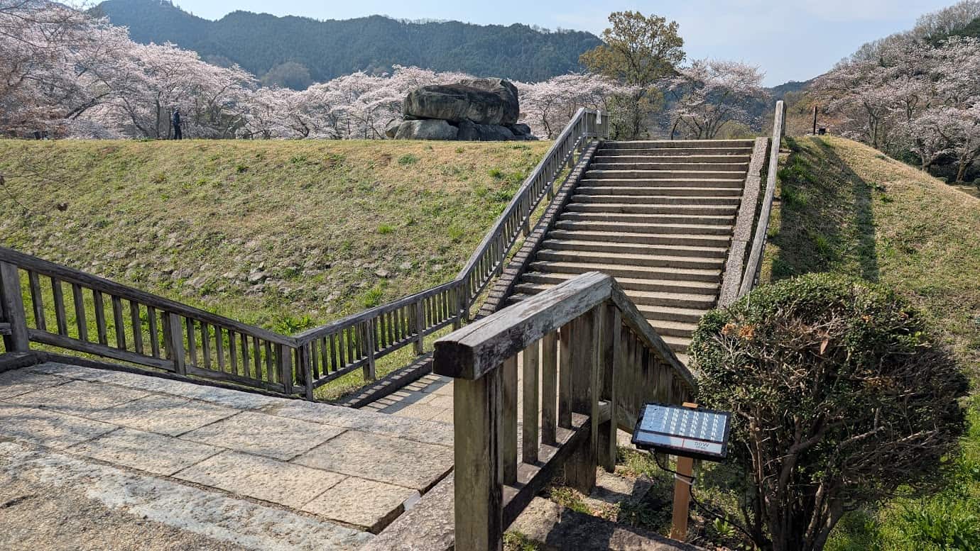 石舞台古墳の受付（拝観受付）を過ぎてすぐにある石造りの階段。段差はそれほど大きくないが、石を敷き詰めた構造で、周囲には緑豊かな風景が広がっている（2026年3月30日撮影）。