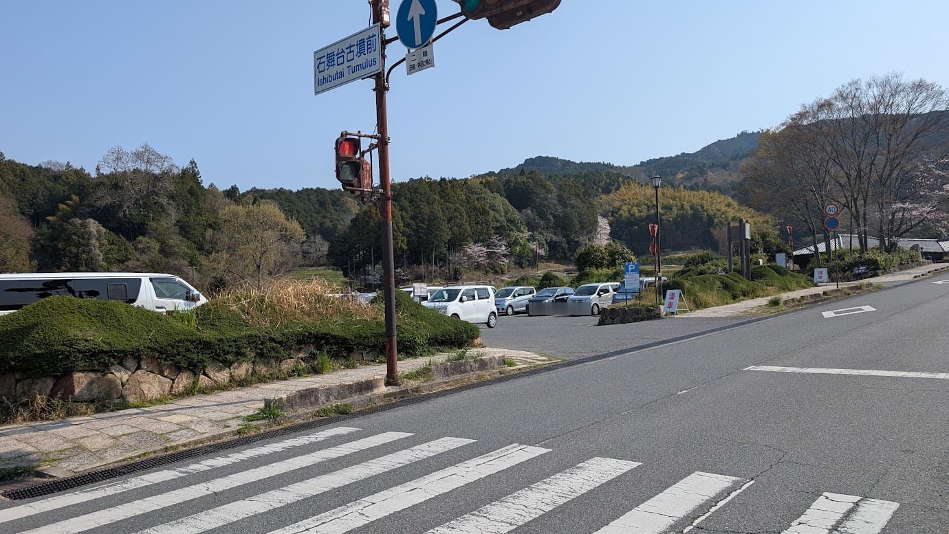 奈良県明日香村、石舞台古墳前の交差点。青空の下、「石舞台古墳前」の標識がある信号機の奥に無料駐車場があり、入り口には「満車」の看板が立てられ、多くの車が停まっている風景（2026年3月30日撮影）。