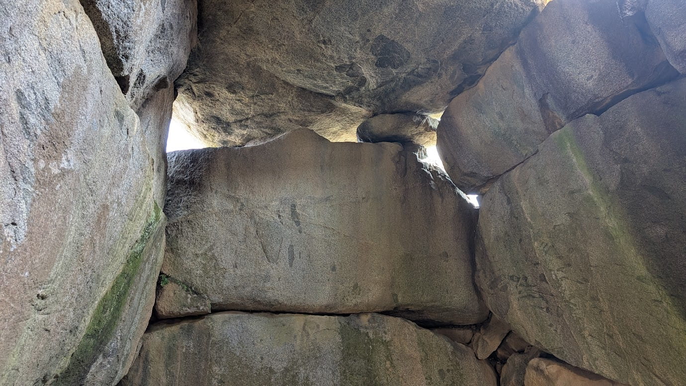 石舞台古墳の石室内部から、1枚目の接合部分を見上げた様子。巨石の隙間から外の光が漏れ、巨大な岩の厚みと、接地面の少なさが強調されている。苔むした岩肌が歴史の深さを物語る（2026年3月30日撮影）。