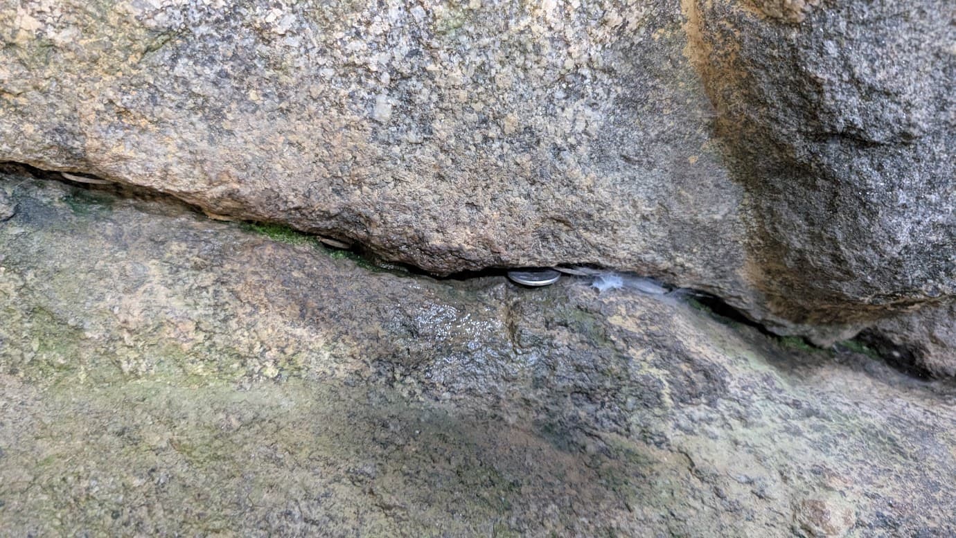 石舞台古墳の石室を構成する巨石のわずかな隙間に、参拝者が挟んでいった硬貨（1円玉や5円玉など）が並んでいる様子。苔むした岩肌に現代のお賽銭が残る不思議な光景（2026年3月30日撮影）。