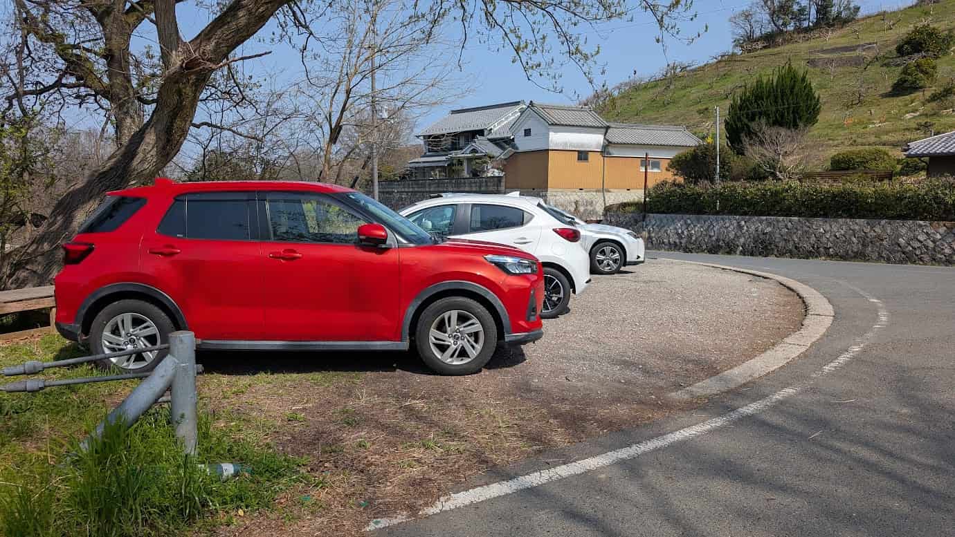 奈良県明日香村、石舞台古墳から徒歩約5分の場所にある舗装された道路。路肩に車1〜2台分が一時的に寄れる程度のスペースがあり、周囲には伝統的な民家と飛鳥の穏やかな山並みが広がっている(2026年3月30日撮影)。
