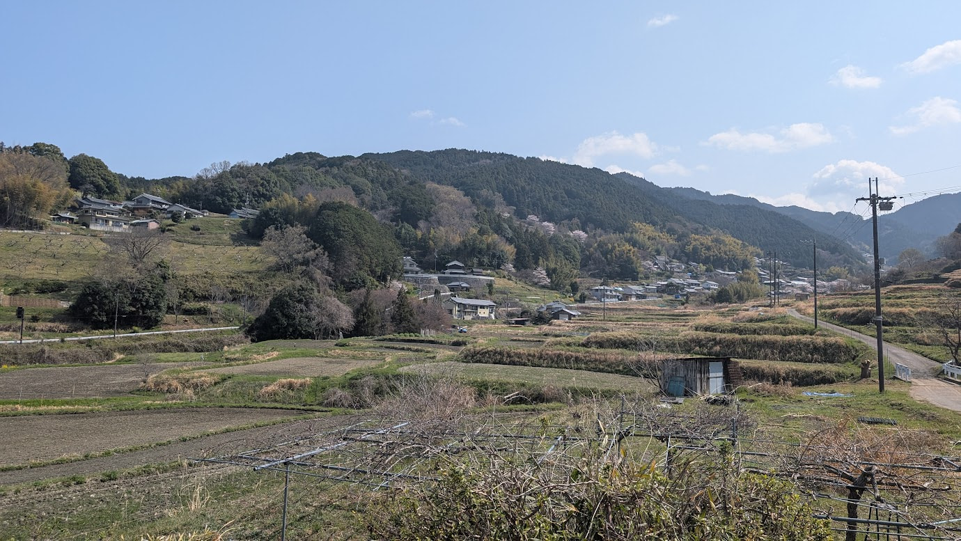 奈良県明日香村、都塚古墳の頂上から見下ろす風景。手前には棚田や飛鳥の民家が広がり、遠くには幾重にも重なる大和の山々と青空が広がるのどかな春のパノラマ(2026年3月30日撮影)。