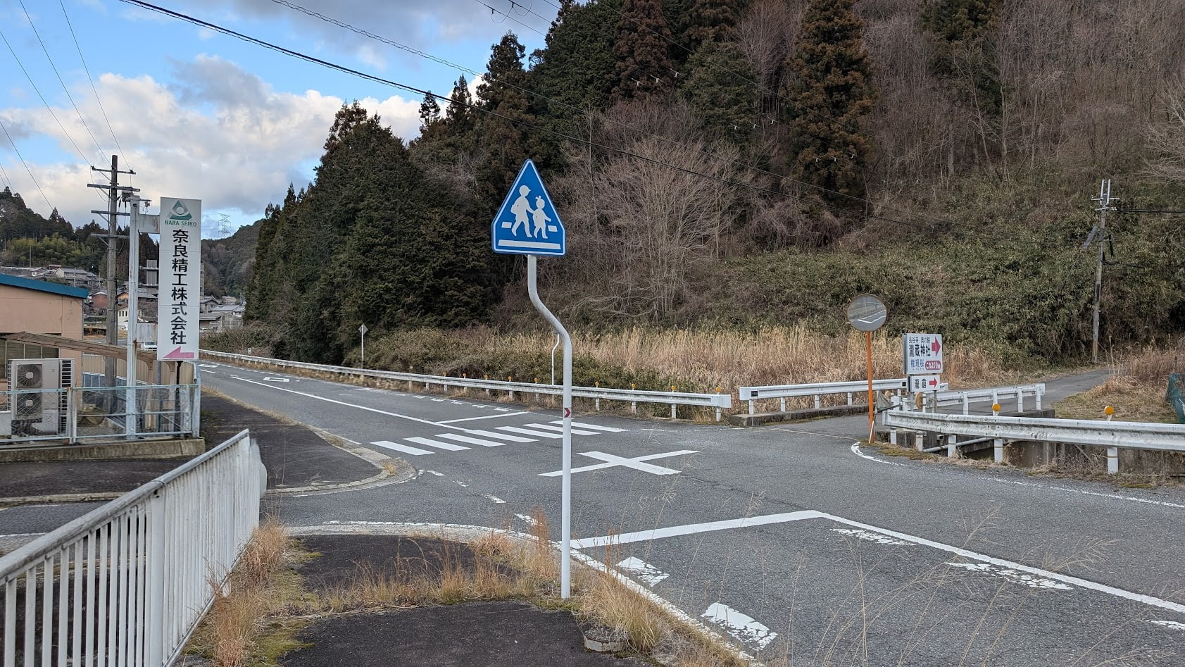 針インター方面の国道沿いにある瀧蔵神社への分岐点。青い空を背景に「瀧蔵神社 ここから1km」と書かれた案内板が立つT字路の風景。