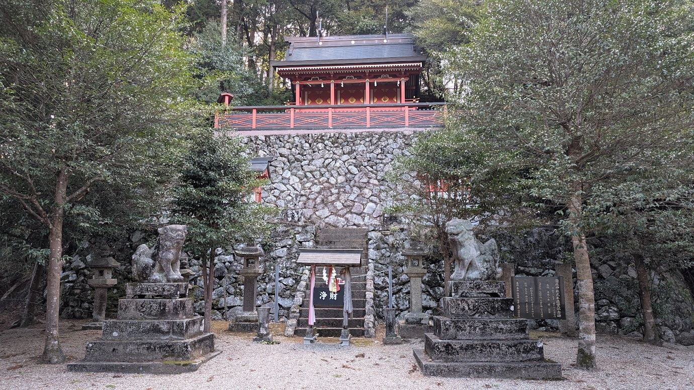 奈良県桜井市・瀧蔵神社。深い木々に囲まれた境内に建つ重厚な本殿と、その前で神域を守るように鎮座する狛犬の全景。