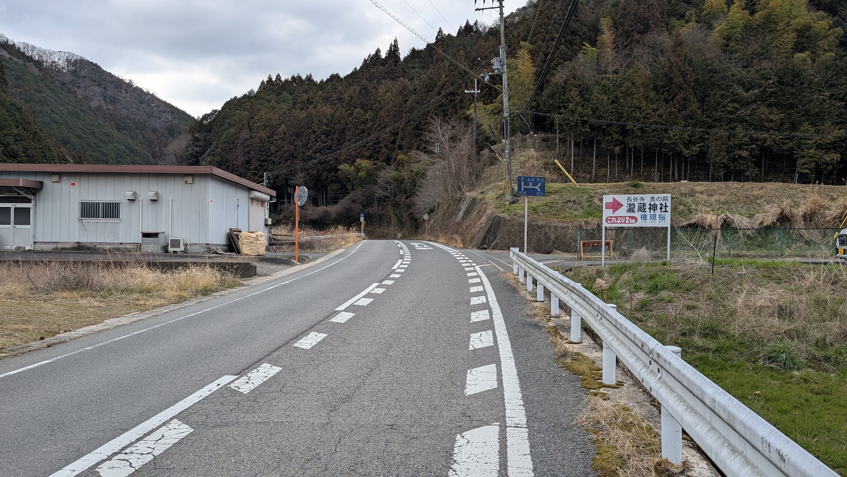 国道165号線沿い、長谷寺方面からの分岐点に立つ「瀧蔵神社 ここから2キロ」の案内看板と、山へと続くT字路の風景。