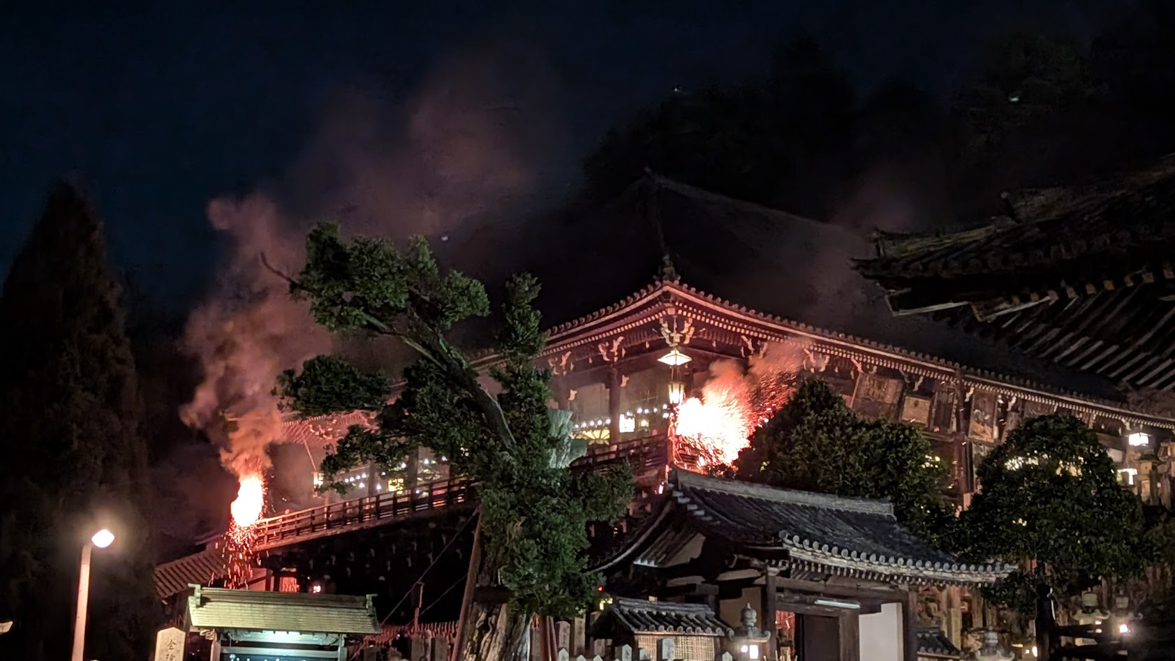 奈良・東大寺二月堂の修二会（お水取り）。舞台の上で2本の巨大な松明が振られ、夜闇に火の粉が舞い散る幻想的な風景。