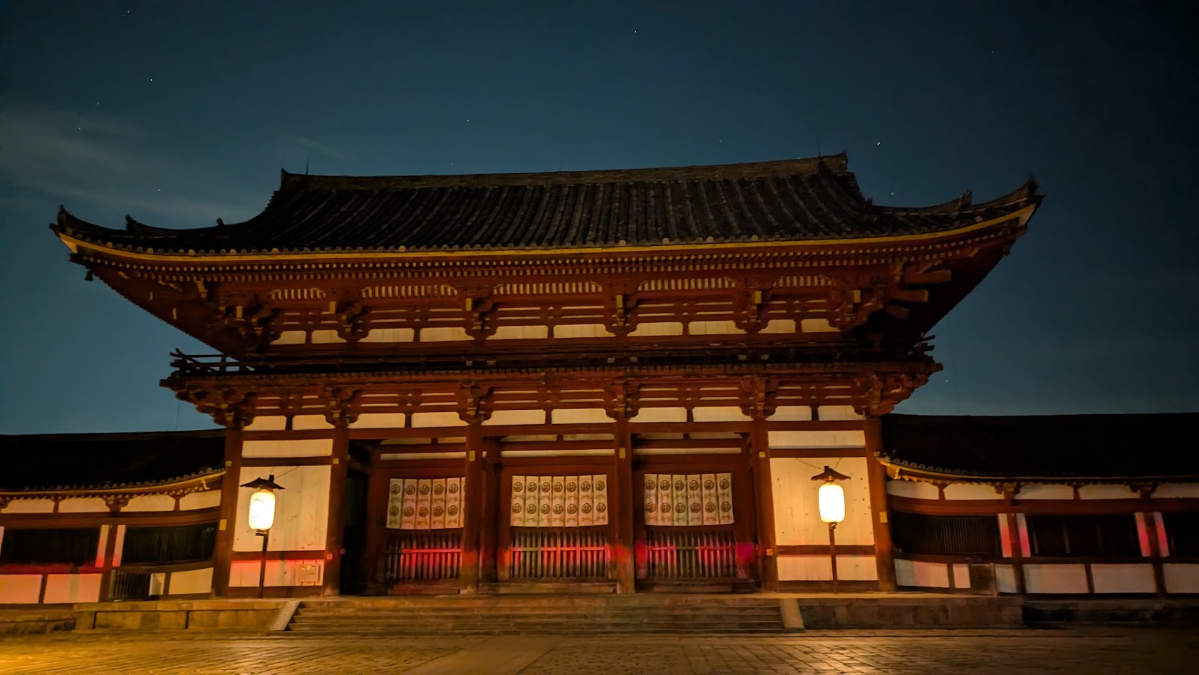 奈良・東大寺の夜の境内。街灯や灯籠の光が石畳をかすかに照らす、静寂に包まれた夜の中門。
