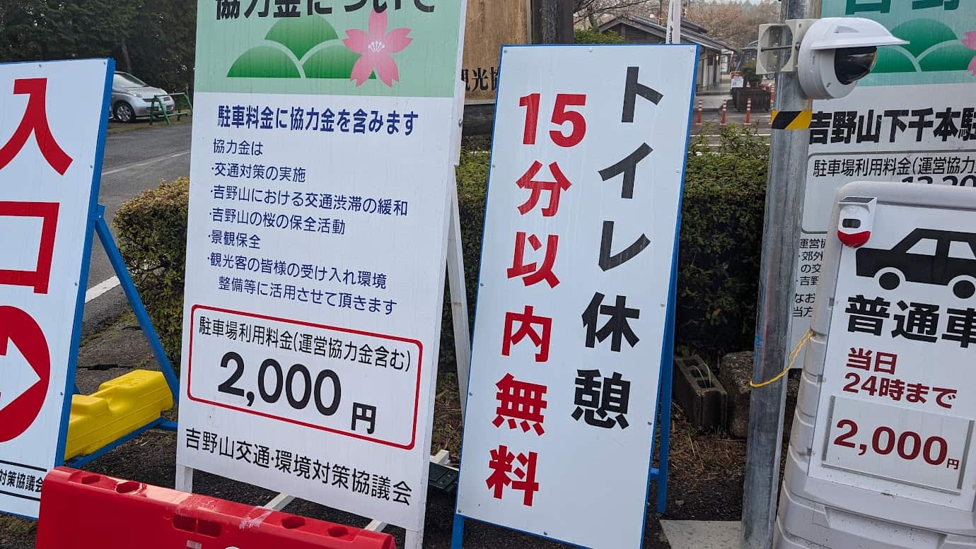 奈良県吉野山の「下千本駐車場」入口にある看板。「15分以内無料」の大きな文字と、駐車料金が桜の保全や交通対策に活用される旨が記載された案内板（2026年3月29日撮影）。