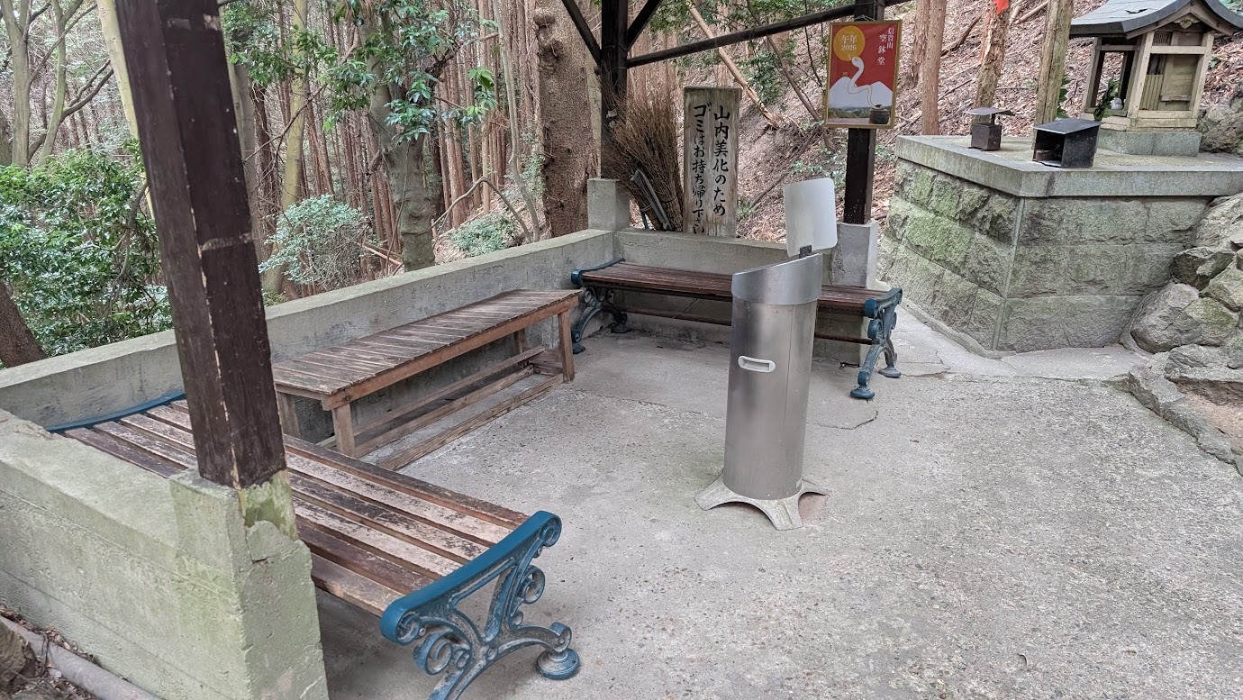 信貴山・空鉢護法堂への山道途中にある休憩所。木造の屋根の下にベンチが並び、灰皿も設置されている。周囲はきれいに掃除・整理整頓されている。