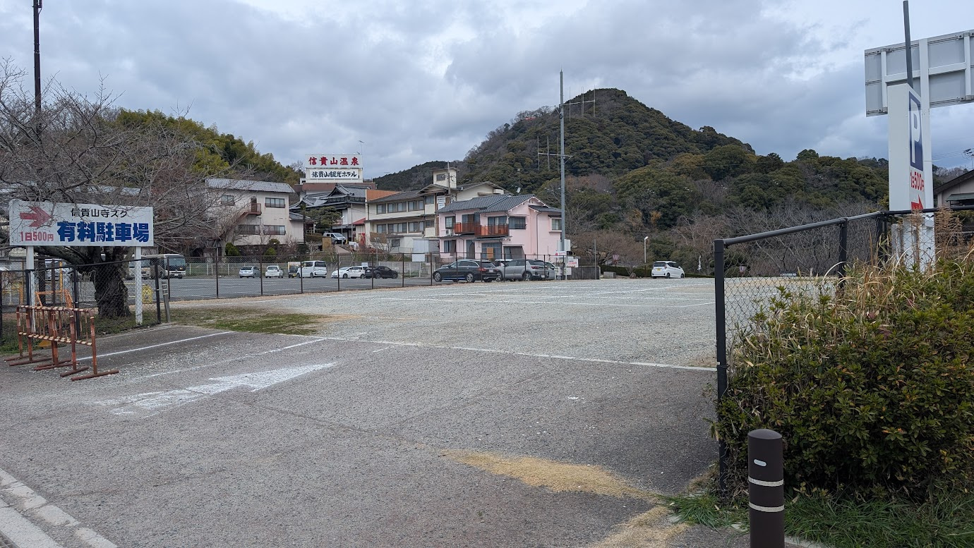 信貴山朝護孫子寺の正門すぐ近くにある、1日500円の砂利敷き駐車場。入口から見た広いスペースで、ロープや白線で区画が仕切られている。