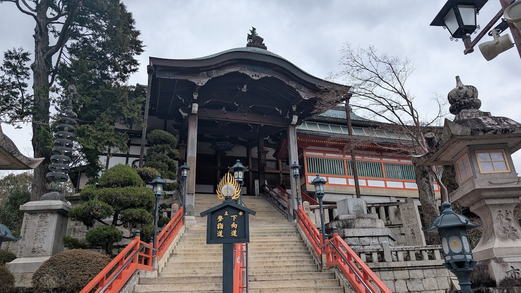 信貴山朝護孫子寺の本堂へと続く長い石段と、その先にそびえ立つ本堂の全景。舞台造りの巨大な木造建築が、山の斜面にせり出すように建っている。